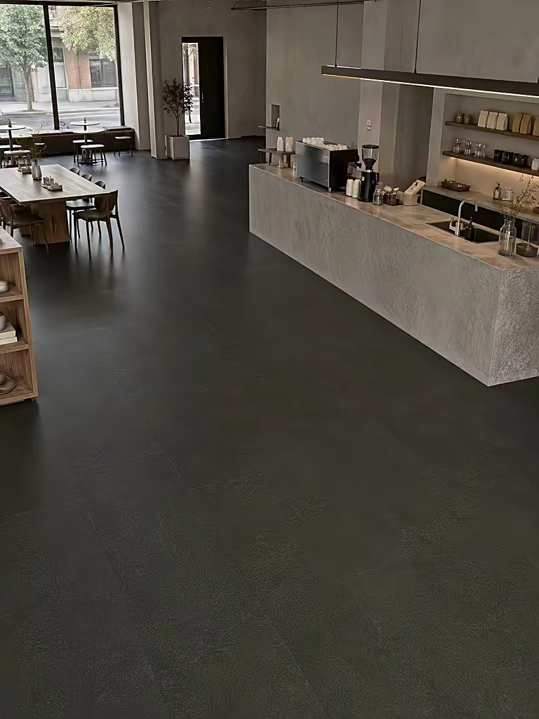 A cafe interior with a dark large-format stone-look floor, timber tables and a stone service counter.