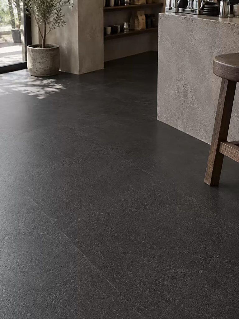 Dark large-format stone-look flooring sweeping towards a seating area and stone counter, with a wooden stool in the foreground.