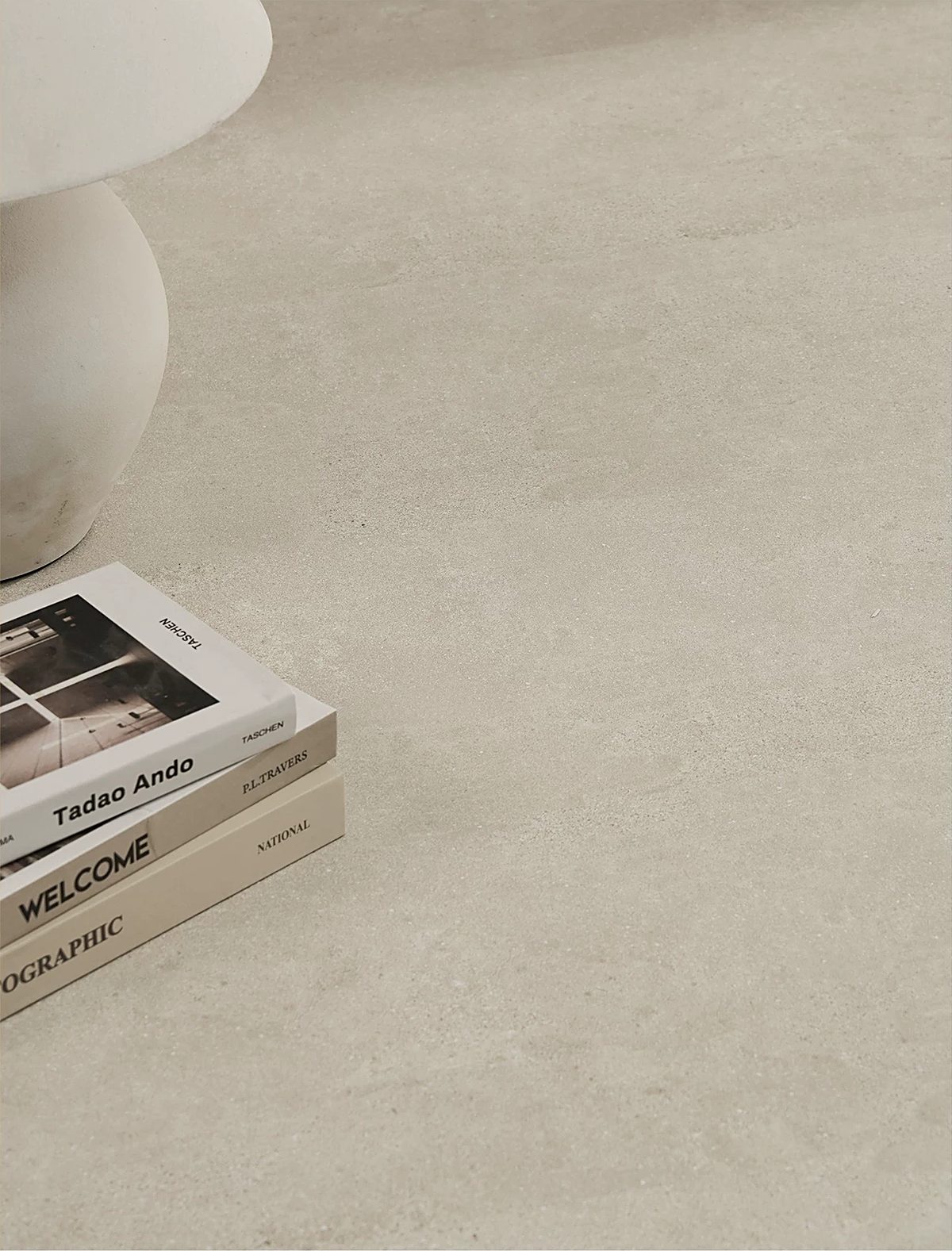 A close view of a pale cream stone-look floor with a stack of design books and the white base of a table beside it