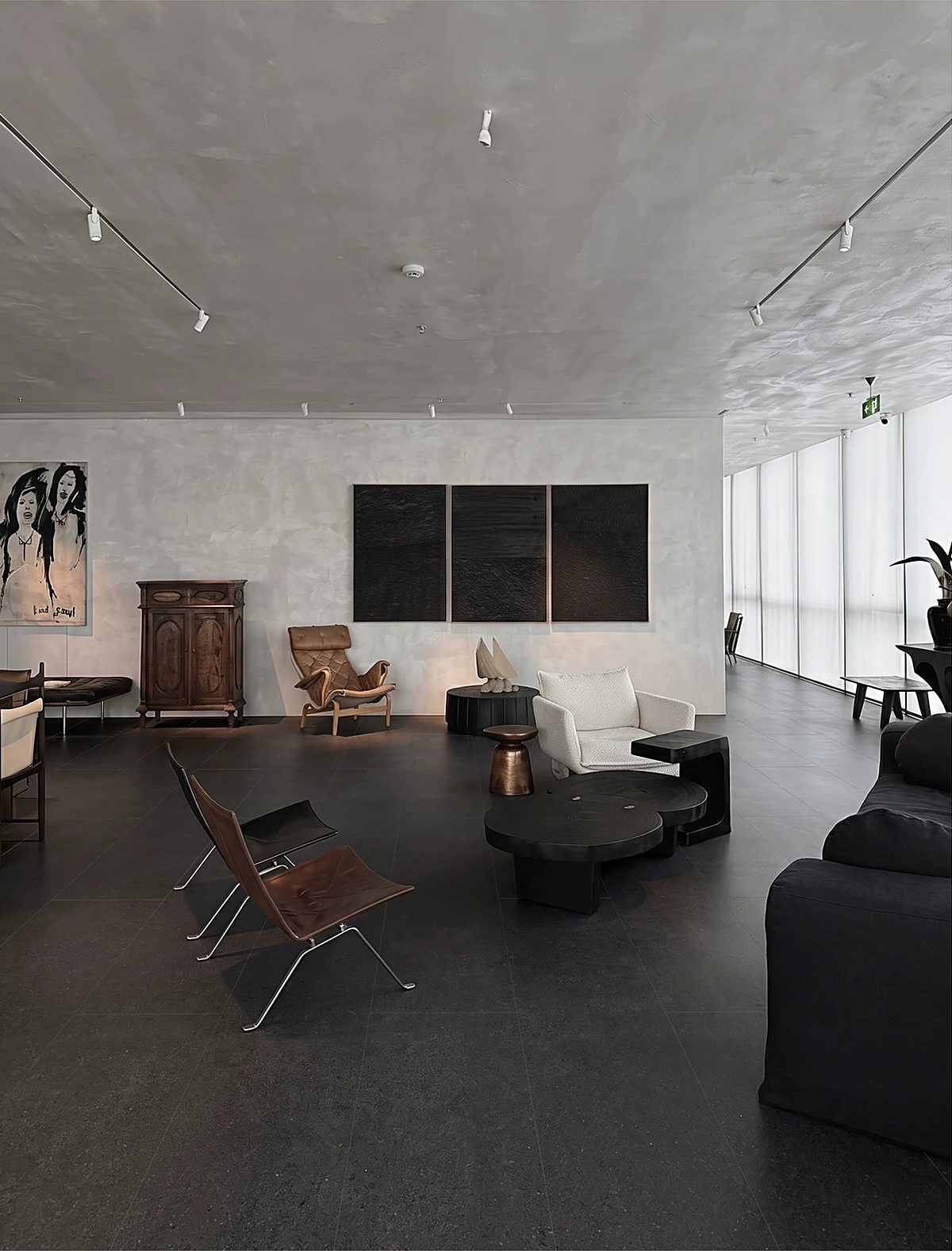A wide sitting room on a dark stone-look floor, lit from full-height glazing