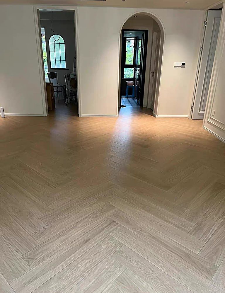 Warm oak herringbone flooring running from the foreground towards an open doorway and hallway.