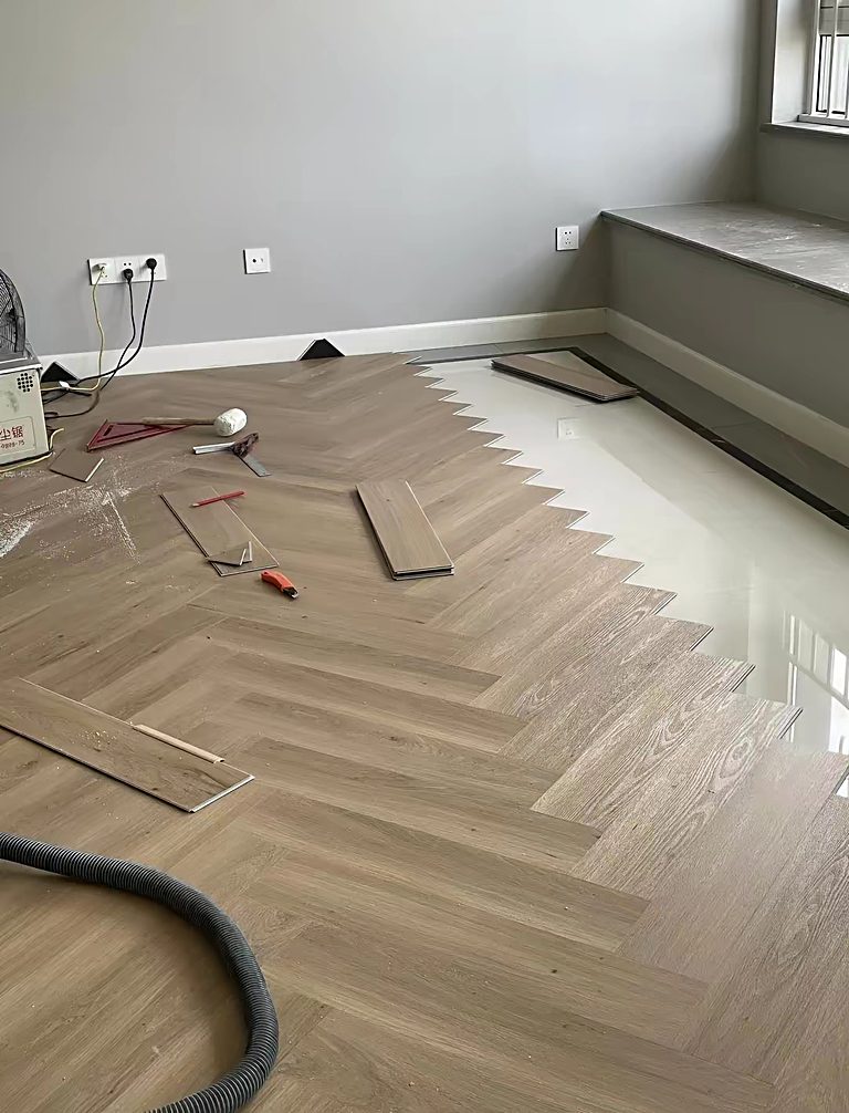 Herringbone flooring part-laid across a room during installation, with the sealed subfloor visible in the foreground.