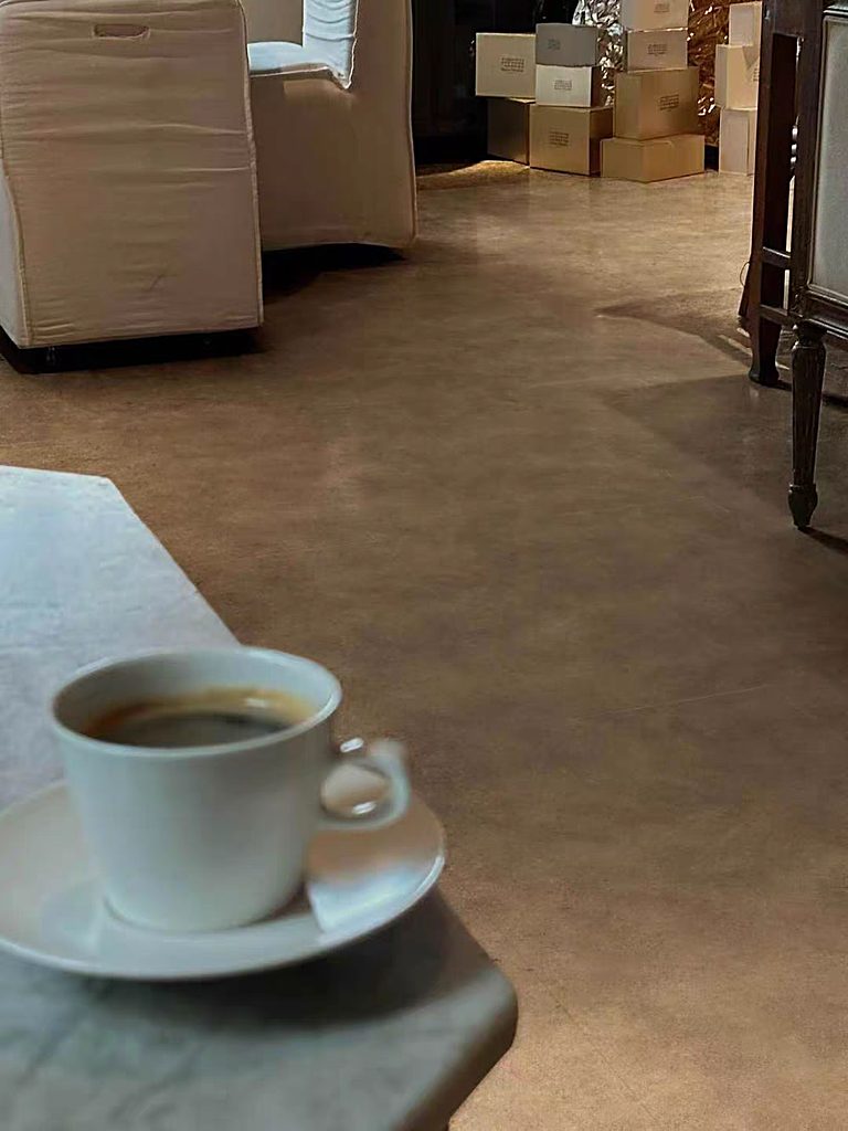 A close view of a smooth stone-look floor beside a low surface with a cup of coffee, looking towards a furnished interior.