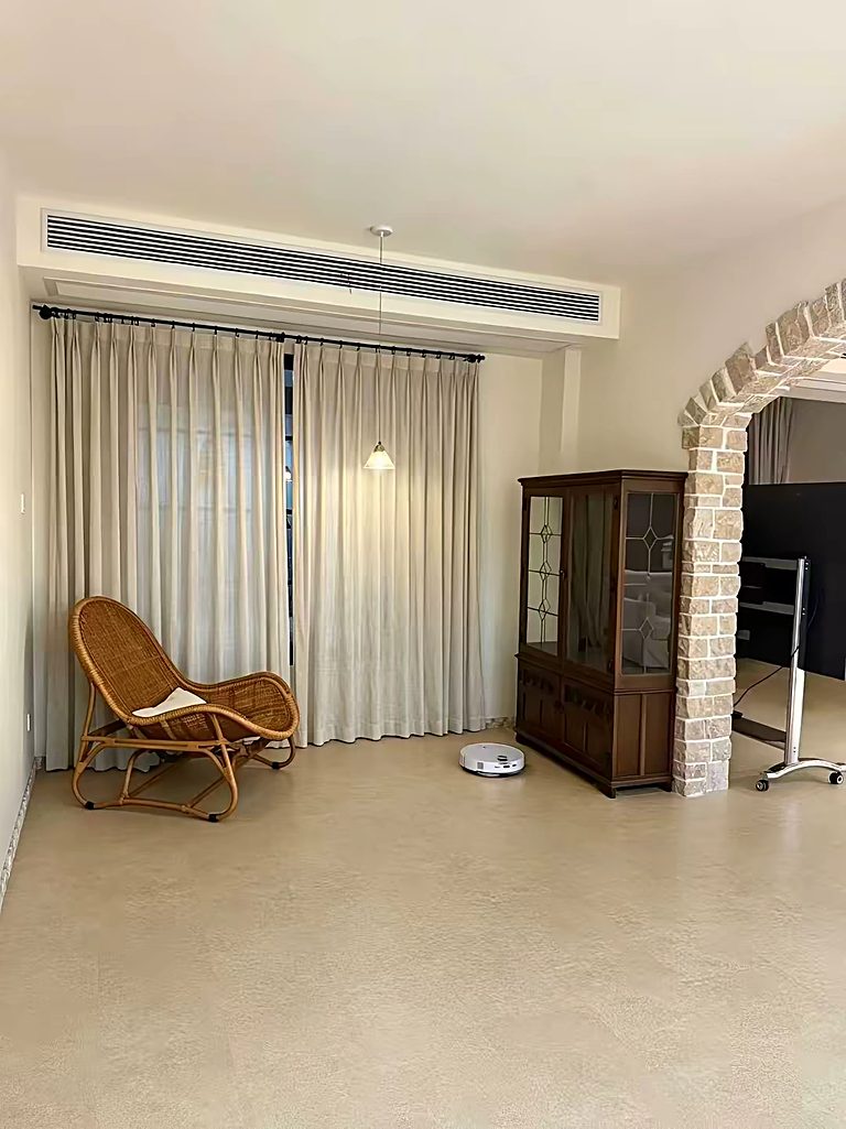 A living space with a smooth stone-look floor, a rattan chair by full-height curtains and a brick archway.