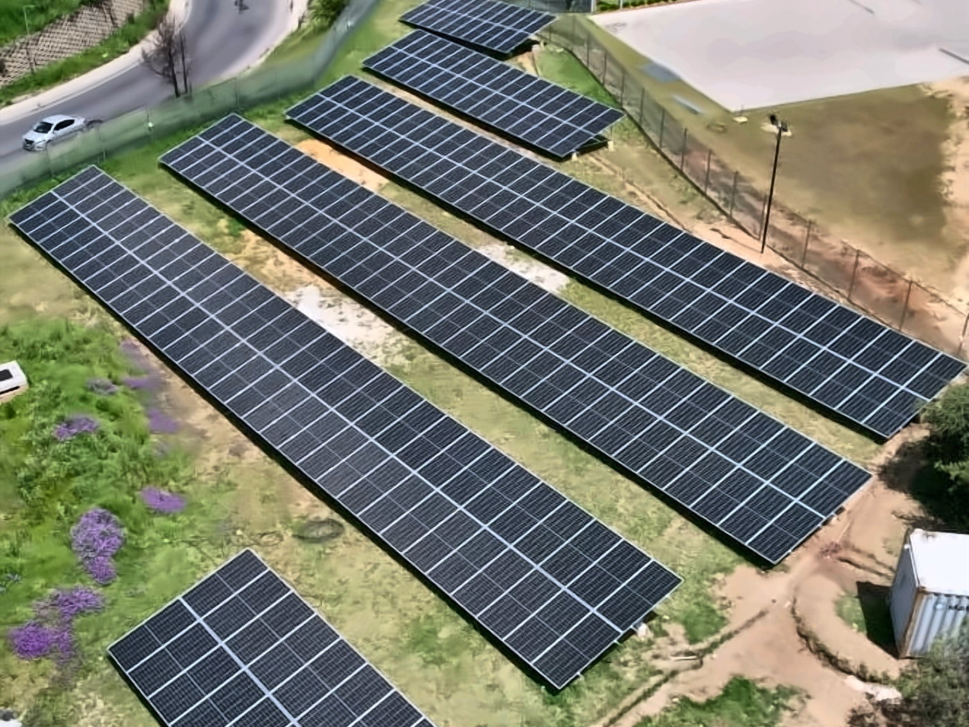 Rows of ground-mounted solar panels beside a commercial facility